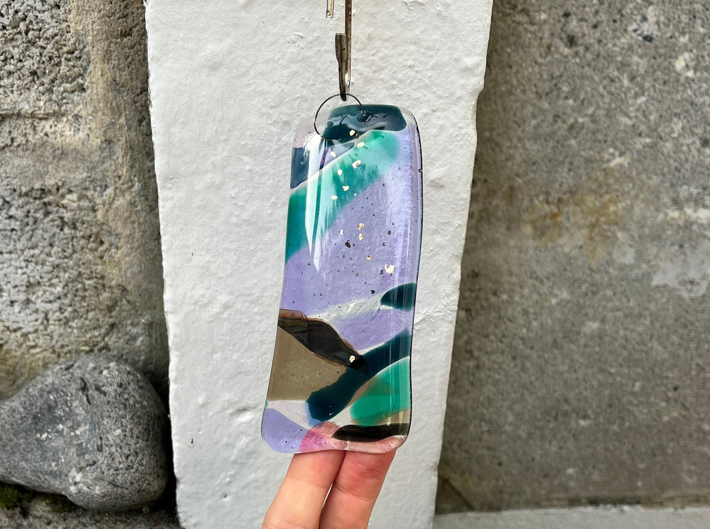 Colorful glass pendant held against a stone wall