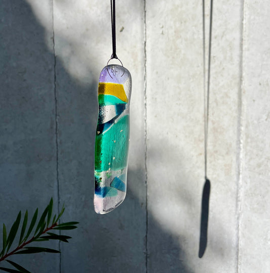 Colorful pendant hanging against a light gray wall with a plant in the corner.