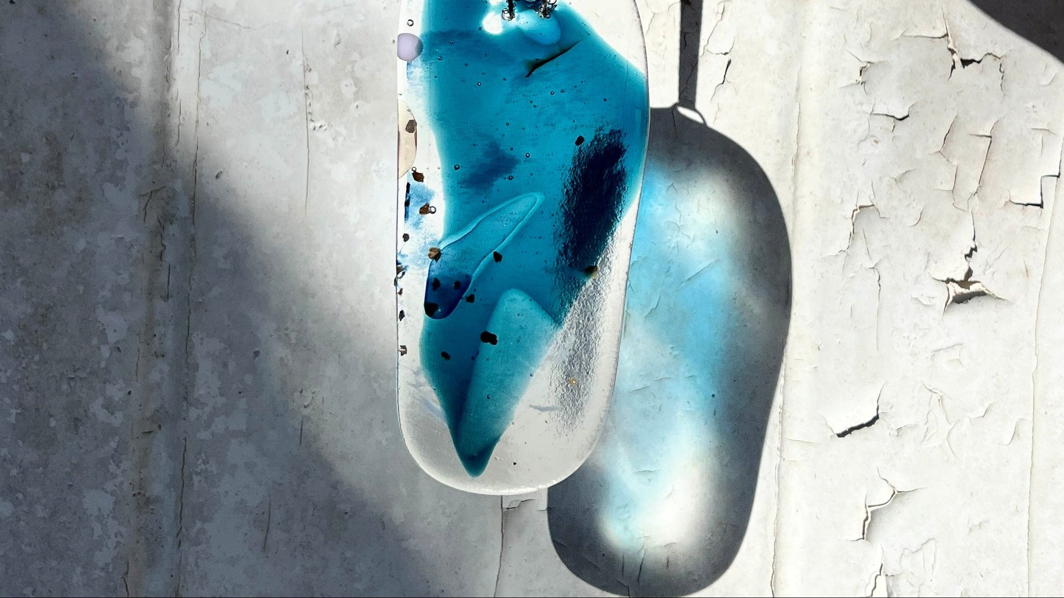 Blue and clear Bryony Lane pendant hanging against a textured wall