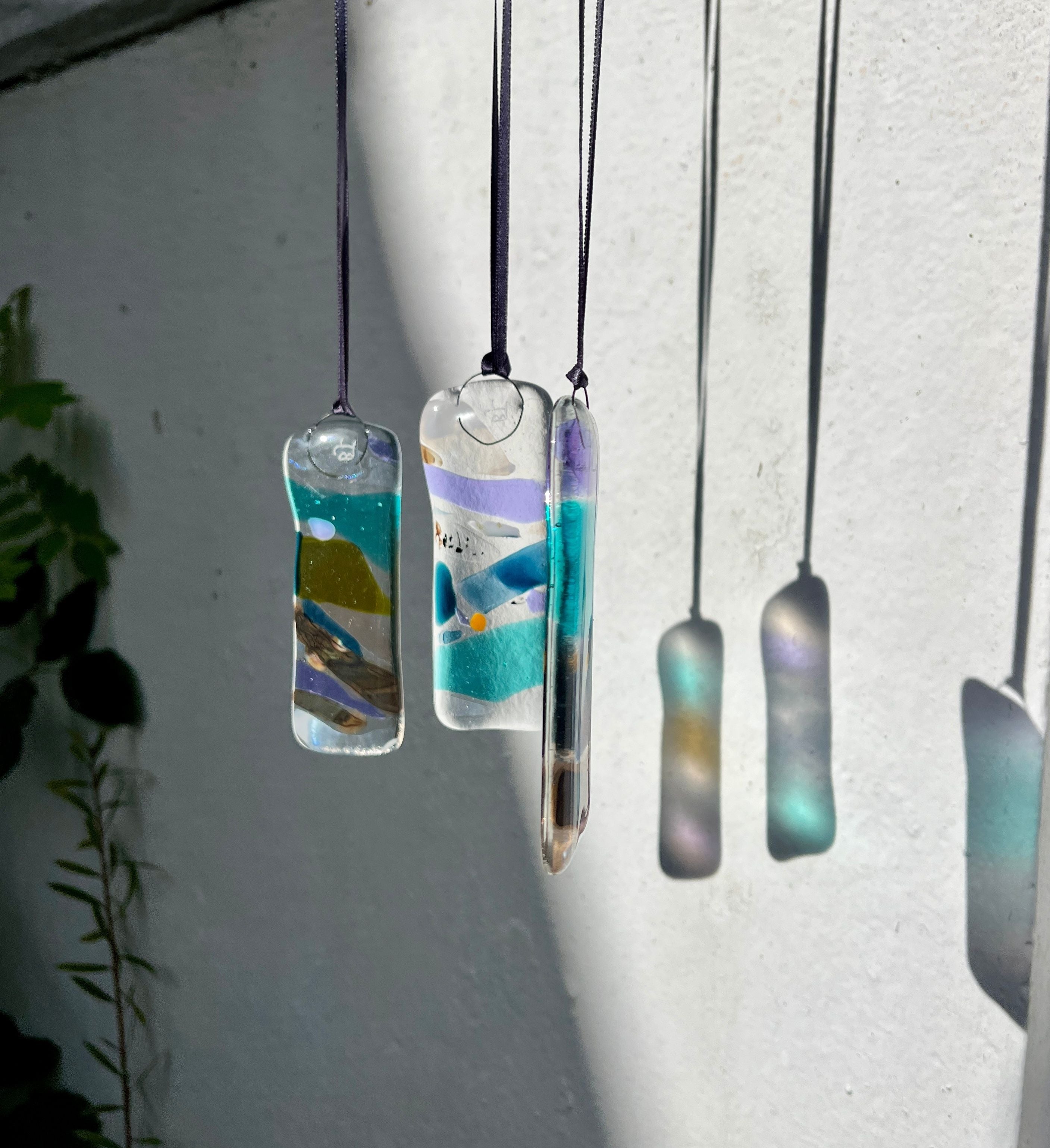 Glass pendants with scenic designs hanging against a white wall.