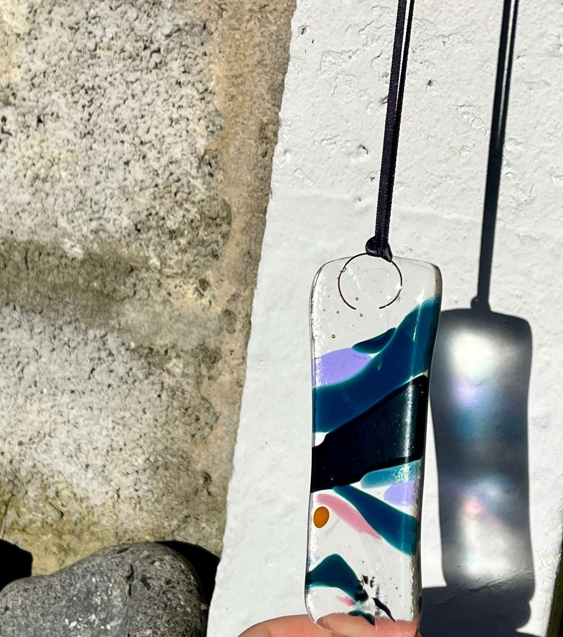 Colorful glass pendant held against a concrete wall