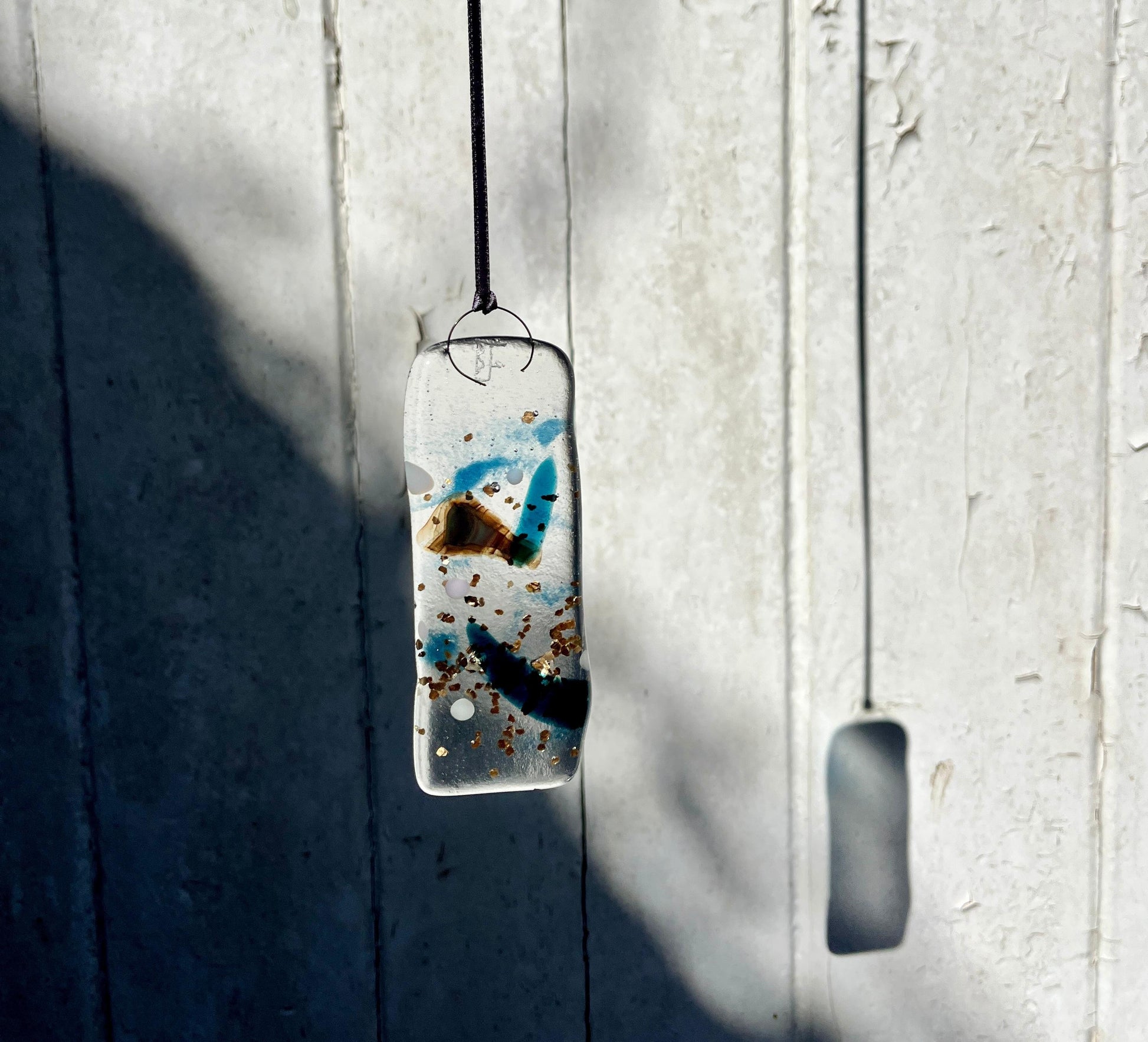 Rectangular pendant with abstract design hanging against a light wooden panel.