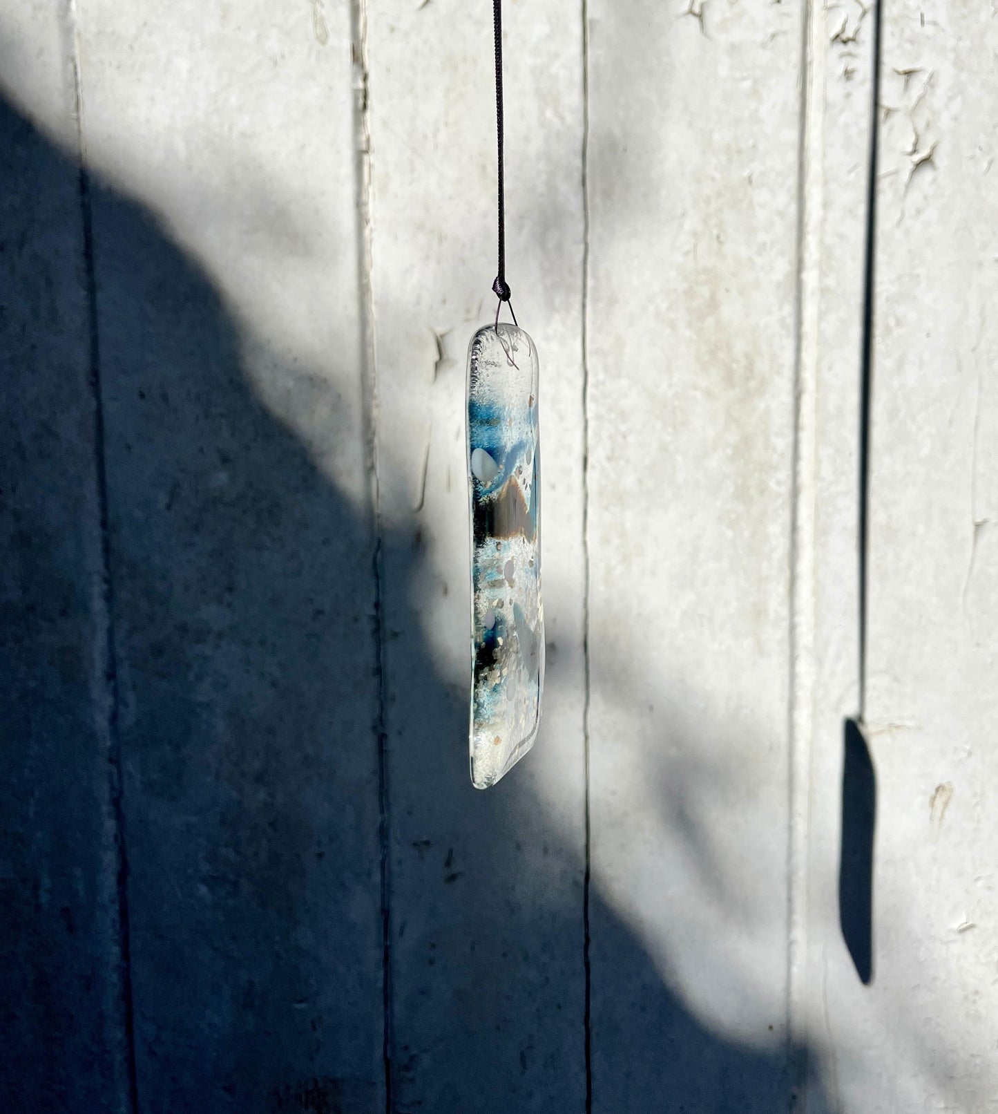Glass pendant with blue and white design hanging against a textured white wall