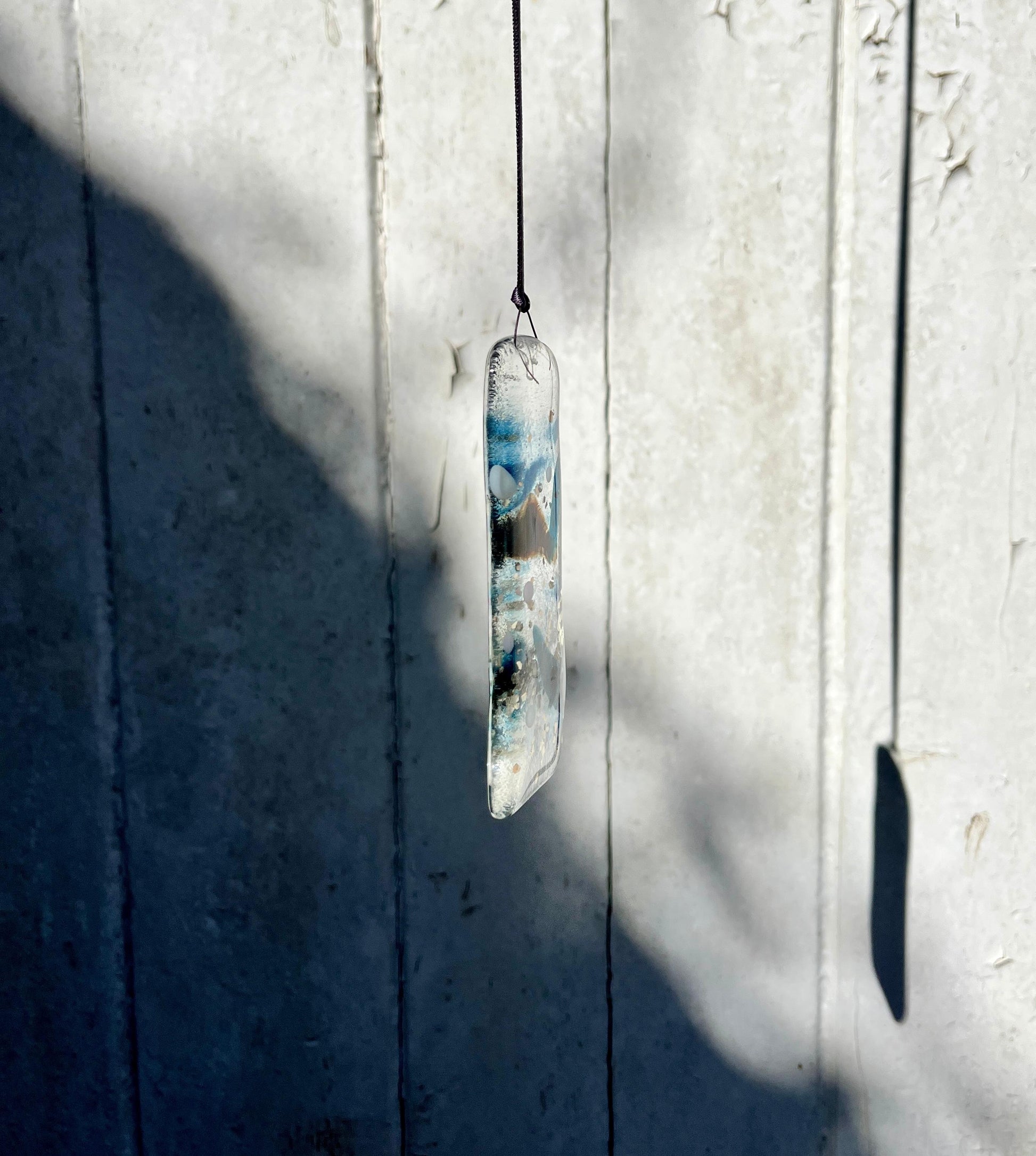 Glass pendant with blue and white design hanging against a textured white wall