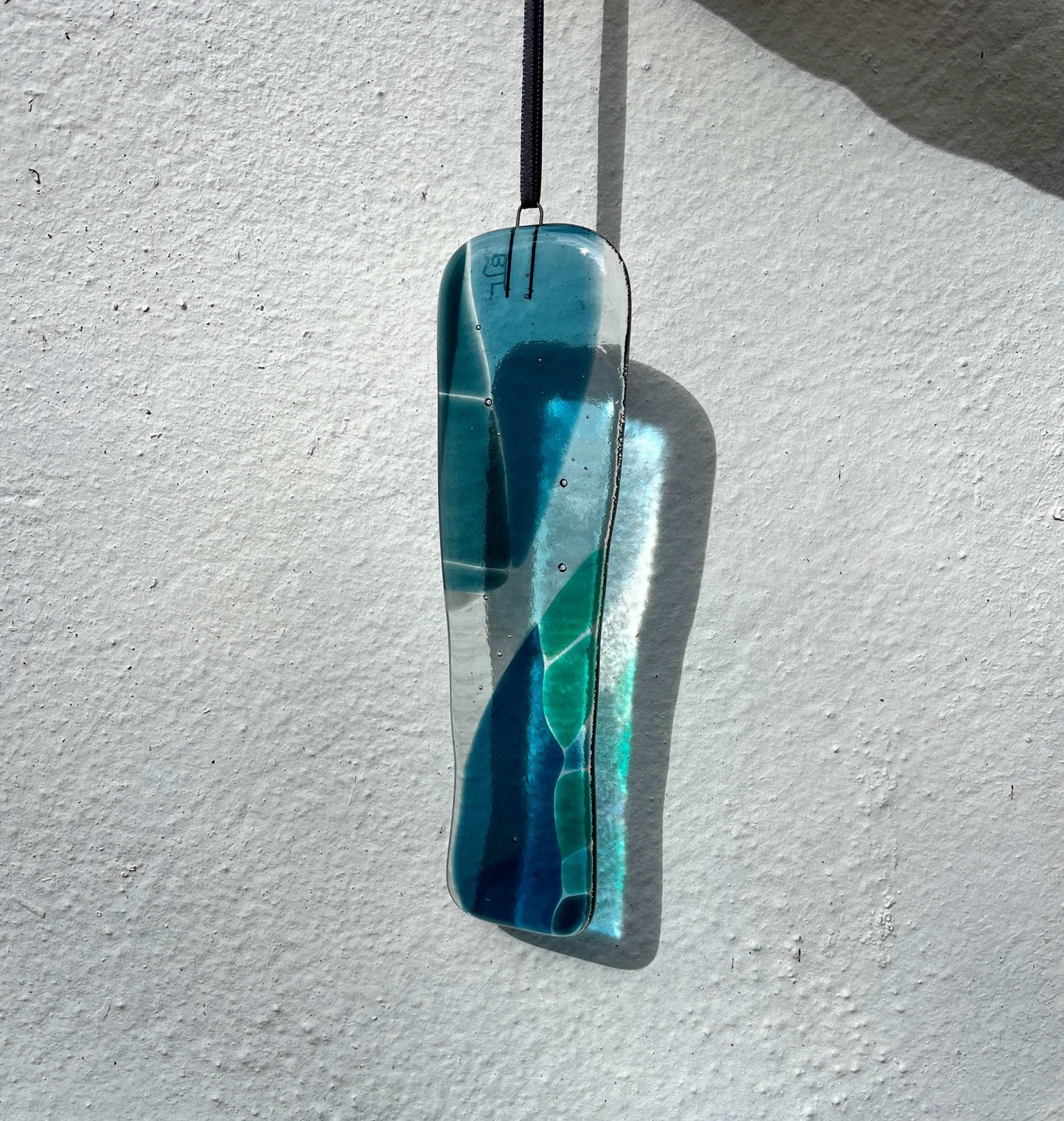 Blue and green glass pendant hanging against a white wall