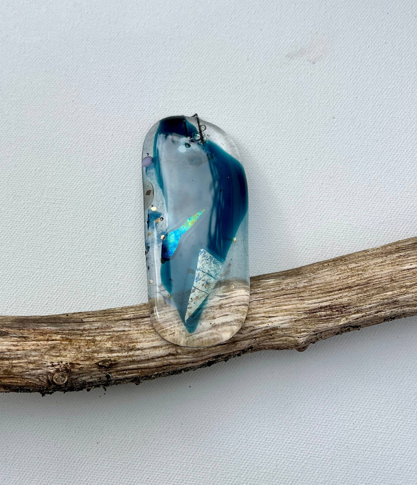 Glass pendant with blue and clear design on a wooden branch against a light gray background