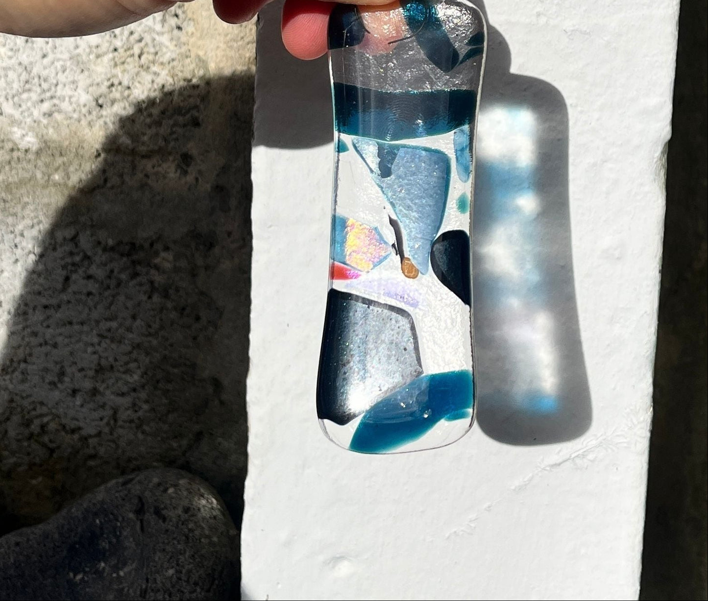 Hand holding a glass pebble with colorful design on a light background