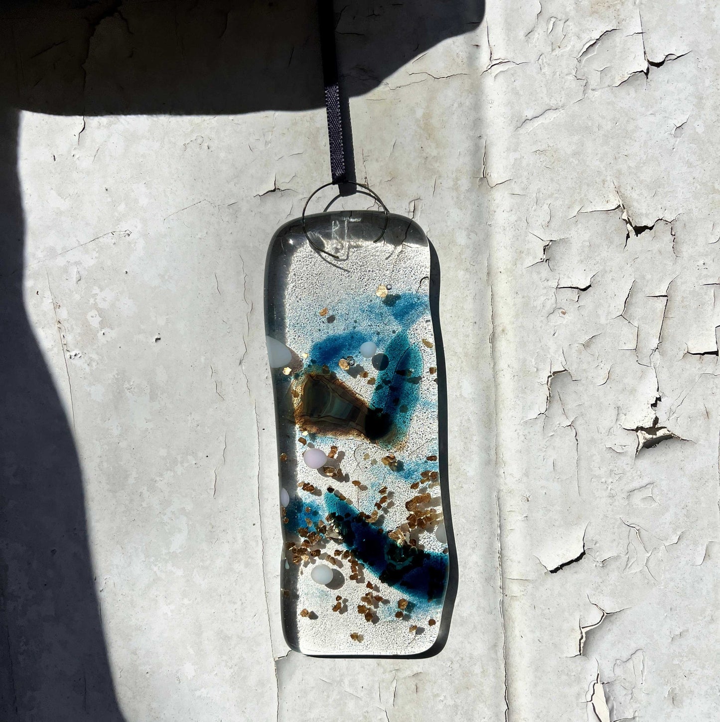 Resin pendant with blue and brown speckles on a textured white surface