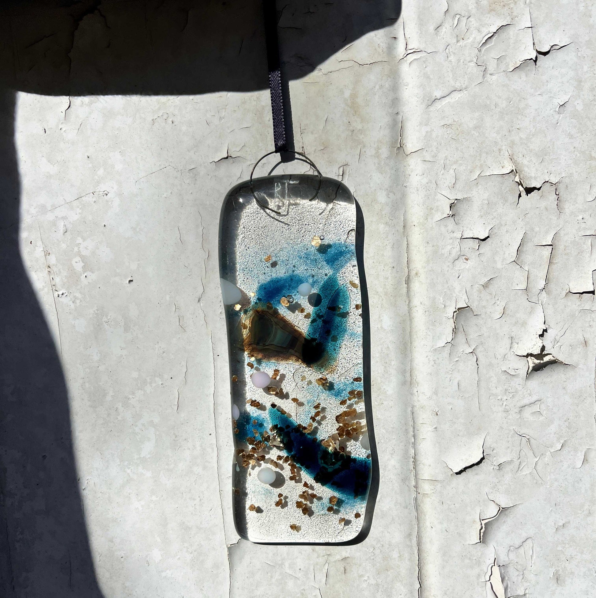Resin pendant with blue and brown speckles on a textured white surface