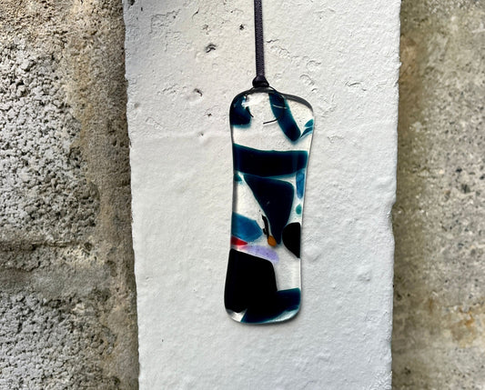 Abstract pendant on a white card against a textured wall background