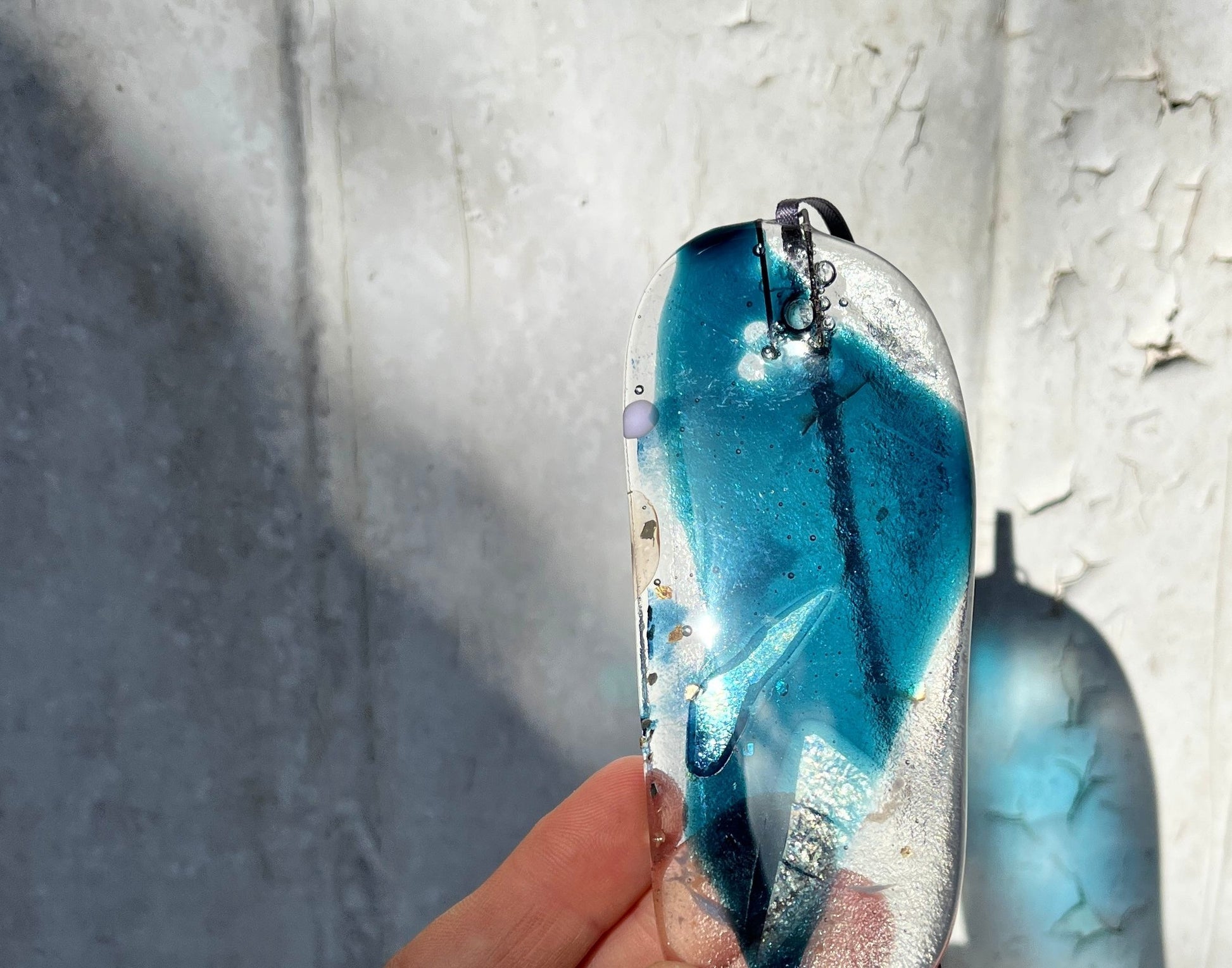 Hand holding a blue and silver pendant against a textured gray background