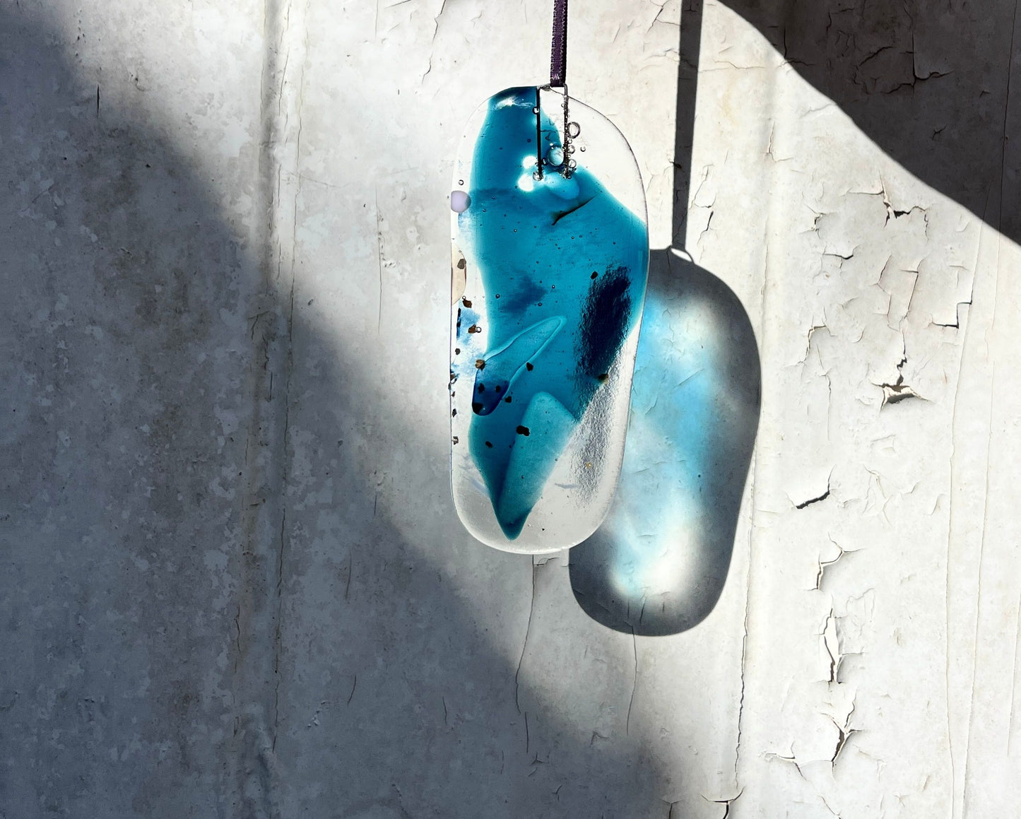 Blue and silver pendant hanging against a textured wall
