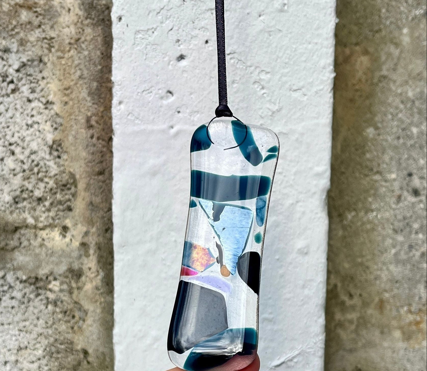 Hand holding a colorful pendant against a stone wall background