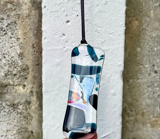 Hand holding a colorful pendant against a stone wall background