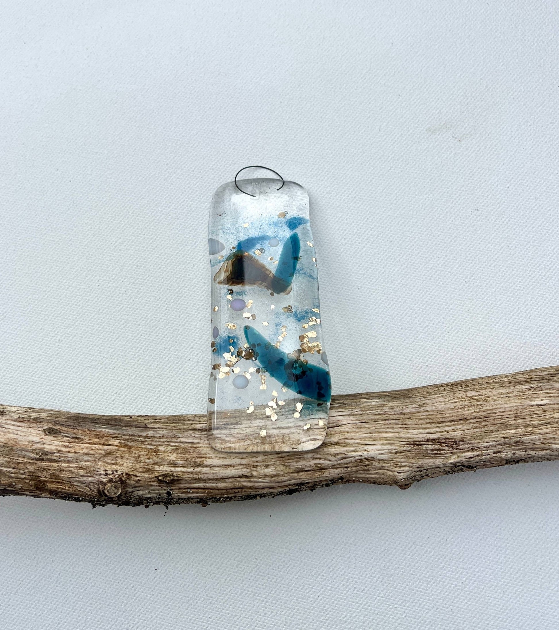Decorative glass pendant with blue and clear design on a branch against a light gray background
