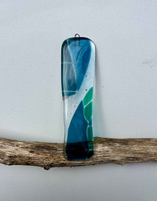 Decorative glass piece with blue and green colors on a branch against a light gray background