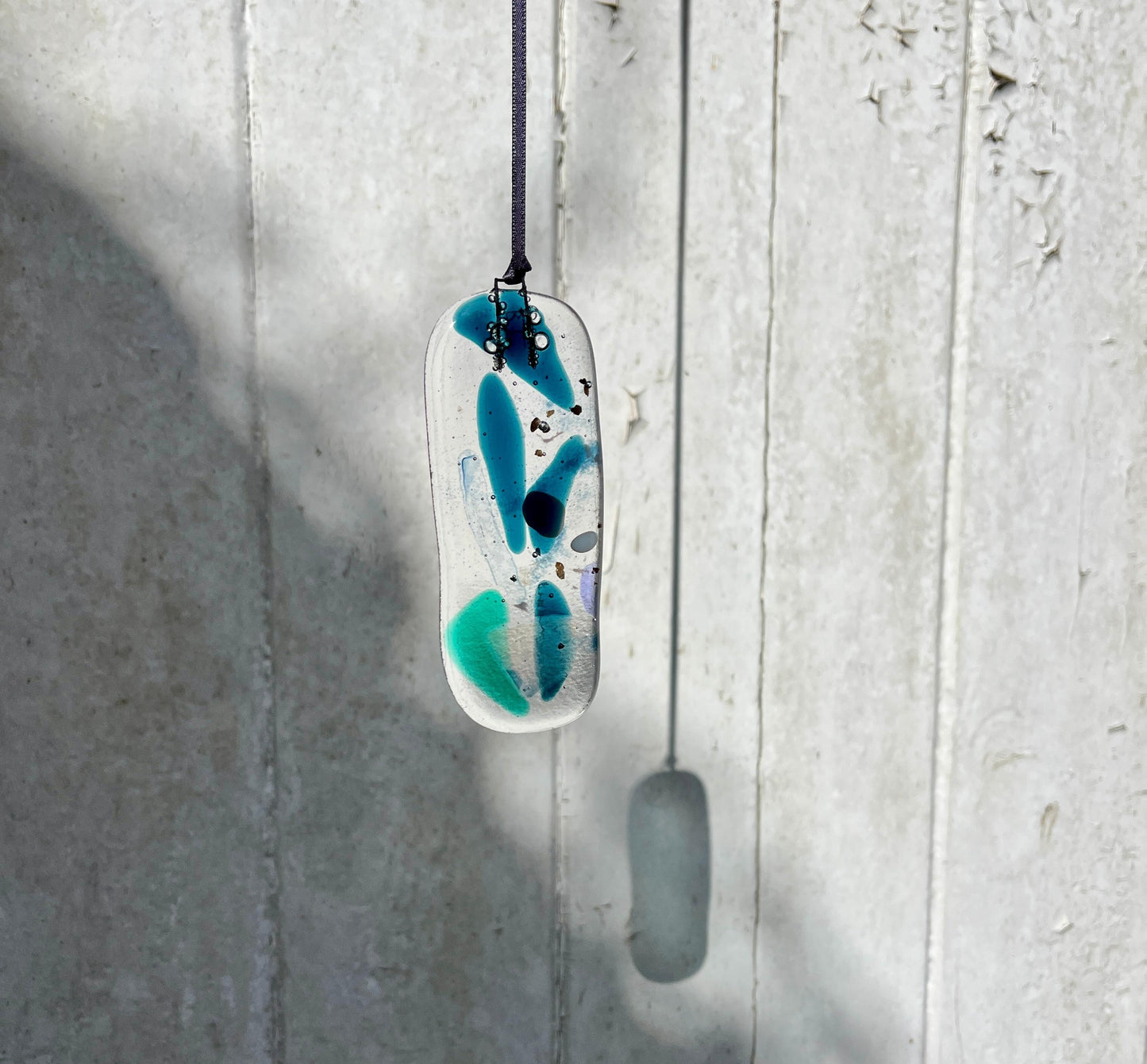 Abstract pendant with blue and green design on a white background