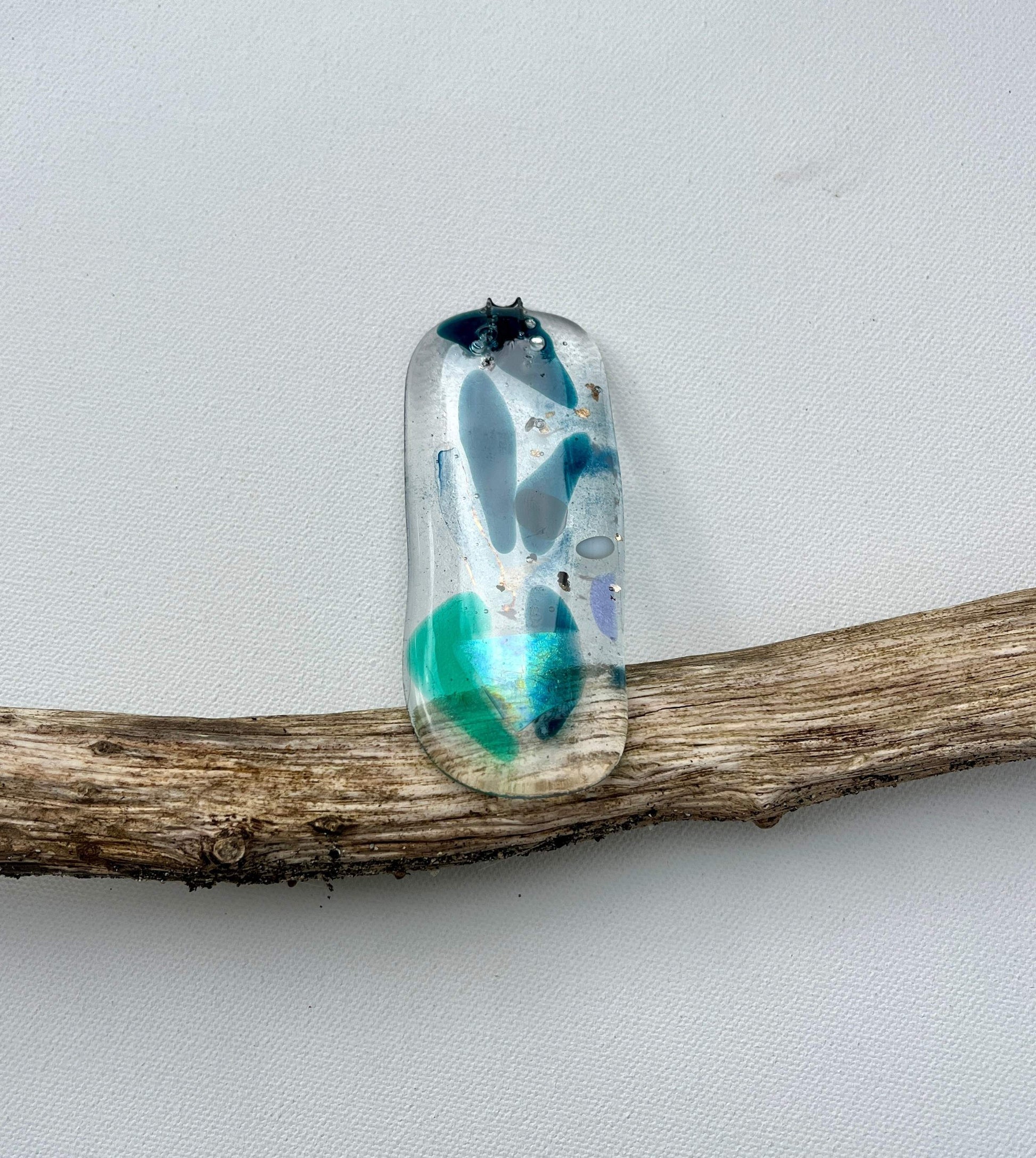 Decorative glass pendant with blue and green design on a wooden branch against a white background